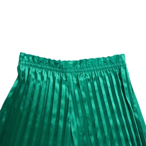 Detail of emerald green pleated pants with elastic waist and shiny satin texture