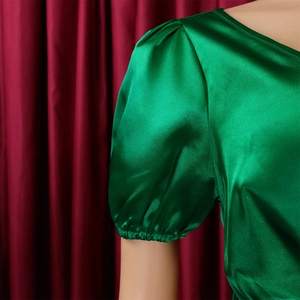 Detail of emerald green satin dress featuring elegant puff sleeves and silky texture
