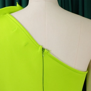 Detail of neon green off-shoulder dress featuring hidden zipper and pleated fabric texture