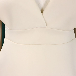 Detalle del escote en V profundo y la banda ancha curva en la cintura del vestido crema