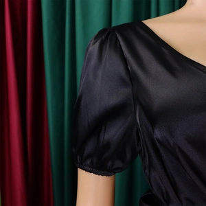 Detail of V-neckline and puff sleeves on a black satin pleated dress with silky texture