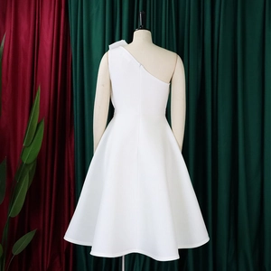 Detail of white one-shoulder dress with bow accent on mannequin against velvet backdrop