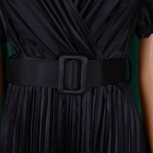 Detail view of black pleated satin dress featuring a V-neck and matching buckled waist belt