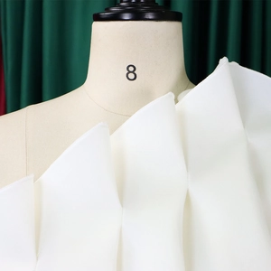 Detail of white off-shoulder evening dress with tiered ruffles and pleated neckline texture