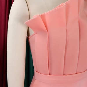Detail of pink one-shoulder dress showing sophisticated pleated texture and matching waist belt