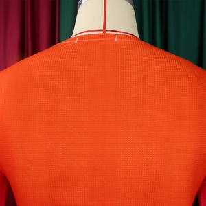 Detailed close-up of bright orange waffle knit fabric texture on a long sleeve top