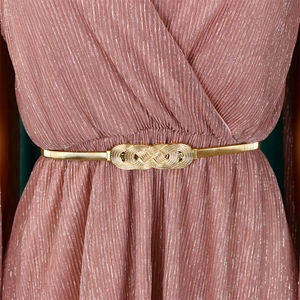 Close-up of gold metal elastic belt with intricate knot buckle on pink pleated dress