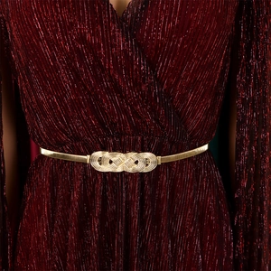Detail of golden elastic belt with infinity buckle on a dark red pleated dress