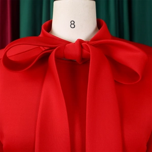 Close-up of a red high-neck dress with a large bow tie and textured crepe fabric
