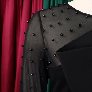 Detail of elegant black mesh jumpsuit featuring intricate beadwork and sheer sleeve panels