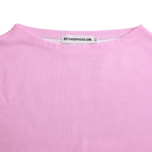 Detail of pink waffle-knit fabric showing texture and Metamorphosis Girl neck label