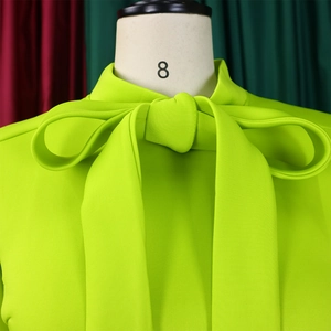 Detail of neon green formal dress featuring a large bow-tie neckline and textured fabric