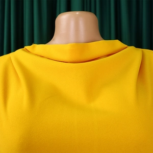 Detailed view of bright yellow dress featuring a cowl neckline and grainy crepe texture