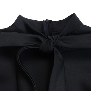 Detail of high neck black top featuring a back zipper and elegant bow tie design