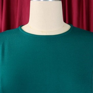 Close-up of the round neckline and dark green pleated fabric texture on the elegant dress