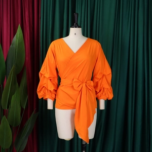 Front view of an orange wrap-around top with puffed sleeves and bow tie detailing