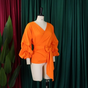 Detail of bright orange wrap top featuring V-neckline and dramatic puff lantern sleeves