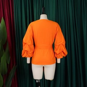 Detail of vibrant orange bubble sleeve blouse with pleated fabric and waist tie