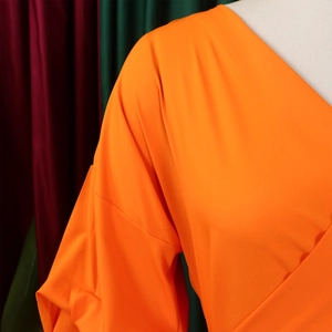 Detail of bright orange v-neck top with pleated puff sleeves on white mannequin