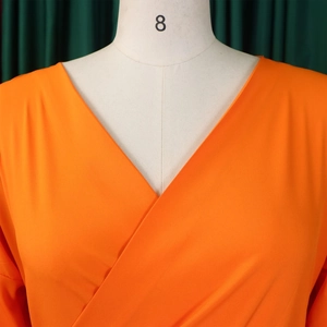 Detail of a bright orange cross V-neck blouse featuring textured fabric and puffy sleeves