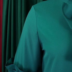 Detail of dark green dress fabric showing ruffled sleeve texture and overlapping collar design