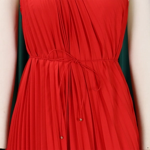 Detailed view of red pleated dress featuring waist tie cord with elegant metal beads