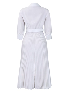 Detail view of the elegant pleated hem and waist belt on a white long sleeve dress