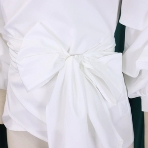 Detail of white off-shoulder top featuring a large waist bow and elegant fabric texture