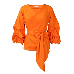 Detail of orange wrap top with elegant V-neck and oversized waist bow tie accent