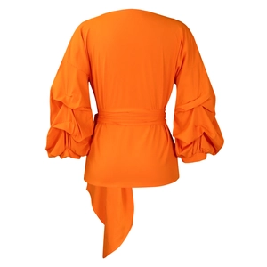 Detail of orange puff sleeve top with cross tie-back design and asymmetrical hem
