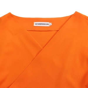 Detailed close-up of V-neck neckline with brand label on orange off-shoulder blouse