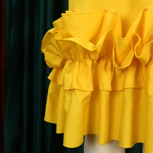 Detail of yellow dress ruffles with small white pearl accents and layered fabric texture