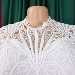 Detail of white lace hollow-out top featuring intricate floral embroidery and wavy high neck