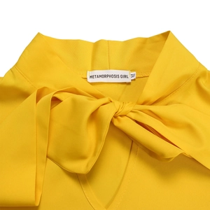 Detail of yellow dress featuring a large bow knot and V-neckline with brand label