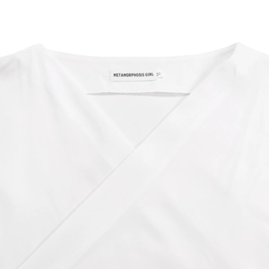 Close-up of V-neck off-shoulder white blouse featuring METAMORPHOSIS GIRL brand label