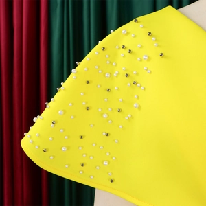 Detail van een gele avondjurk met witte parels en zilveren metalen studs op de schouder