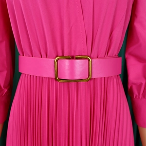 Detail of fuchsia pleated dress featuring a wide belt with gold buckle and waist cinching