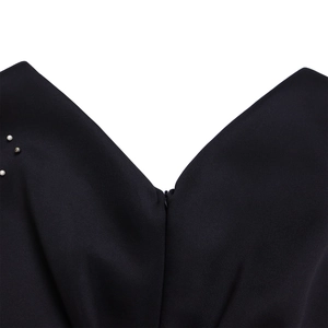 Detailopname van de V-hals met subtiele parelaccenten en zwart getextureerd materiaal