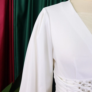Dettaglio della tuta bianca con scollo a V, maniche a sbuffo, perle e strass