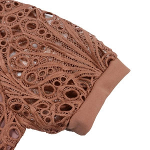 Detailed close-up of brown geometric lace stitching and textured pleated fabric on dress