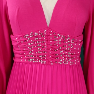 Dettaglio della cintura in vita con perle bianche e strass su tuta plissettata color fucsia