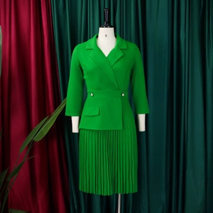 Detail van groene jurk met lange mouwen, reverskraag en plooirok op een etalagepop
