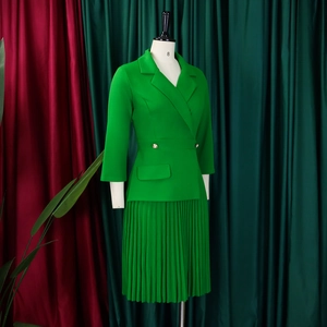 Detail van groene geplooide jurk en blazer met lange mouwen en gouden knopen