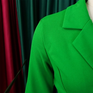 Detailopname van de grasgroene blazer met reverskraag en fijne geweven textuur van stof