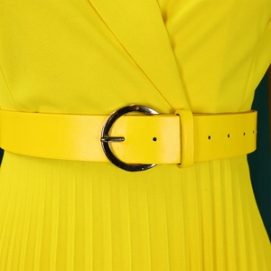 Détail de robe plissée jaune vif avec ceinture à boucle argentée ronde à la taille