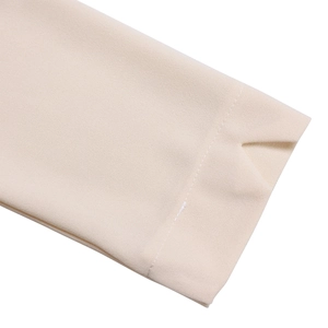 Détail de la manche d'une robe beige avec poignet en V et surpiqûres blanches nettes