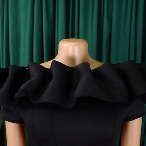 Dettaglio dello scollo nero a barca con eleganti balze decorative sulla spalla