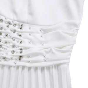 Dettaglio di una tuta bianca con pieghe intricate, perle decorative e strass lucenti