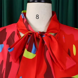 Détail du chemisier rouge fleuri avec col à nœud élégant et manches bouffantes