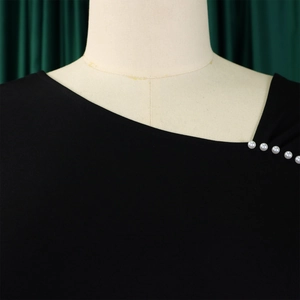Detail van elegante zwarte jurk met asymmetrische halslijn en decoratieve parelknopen